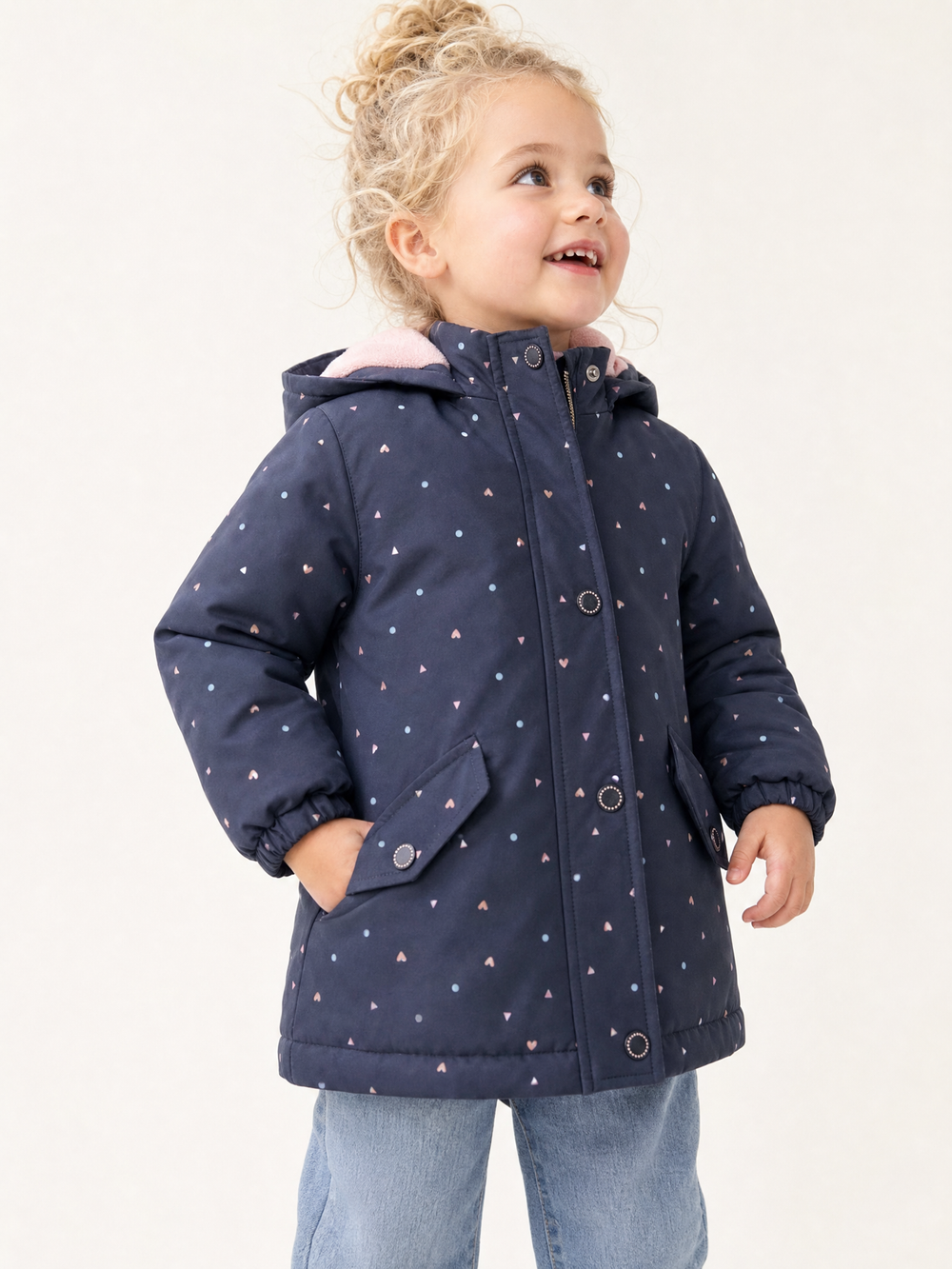 Young blonde girl wearing a navy heart print hooded zip jacket in a bright studio
