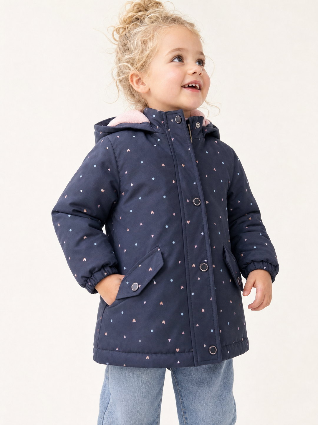 Young blonde girl wearing a navy heart print hooded zip jacket in a bright studio