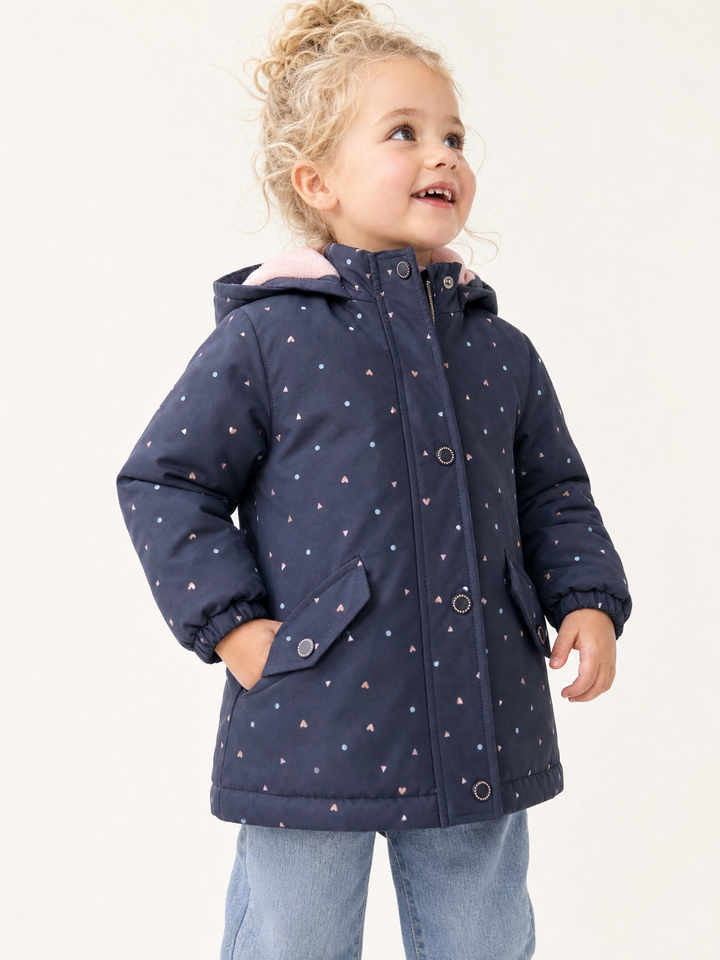 Young blonde girl wearing a navy heart print hooded zip jacket in a bright studio