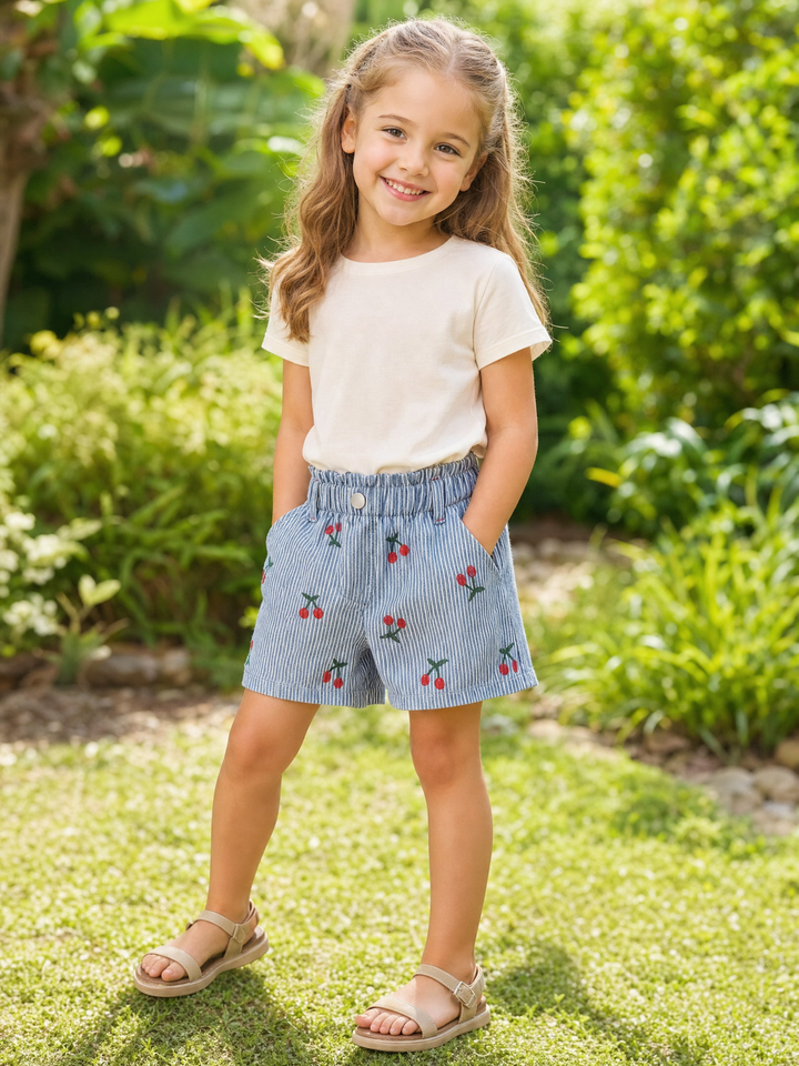Girl wearing blue and white cherry stripe cotton shorts in a summer garden